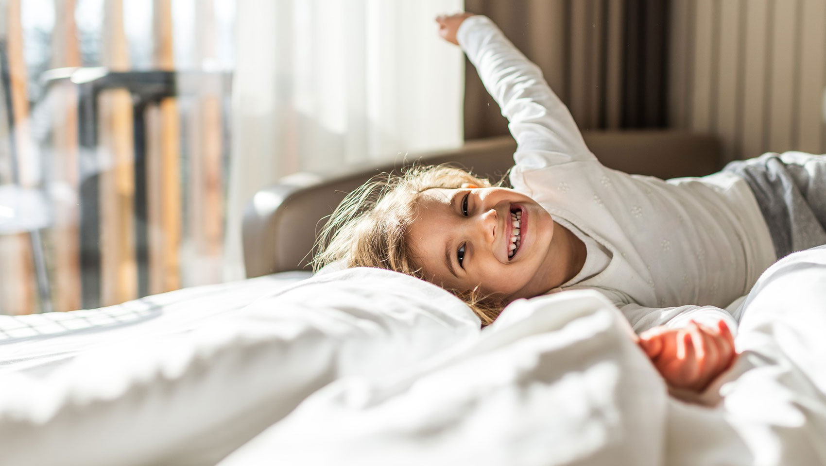 A small child, lying on a bed, smiling at the camera