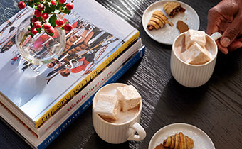 Hot Cocoa, cookies, books, and holly on a table