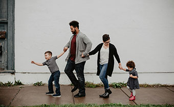 A young boy, a father, a mother, and a young girl all walk in a line holding hands