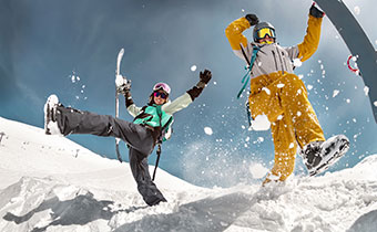 two skiers kicking up snow and holding skis